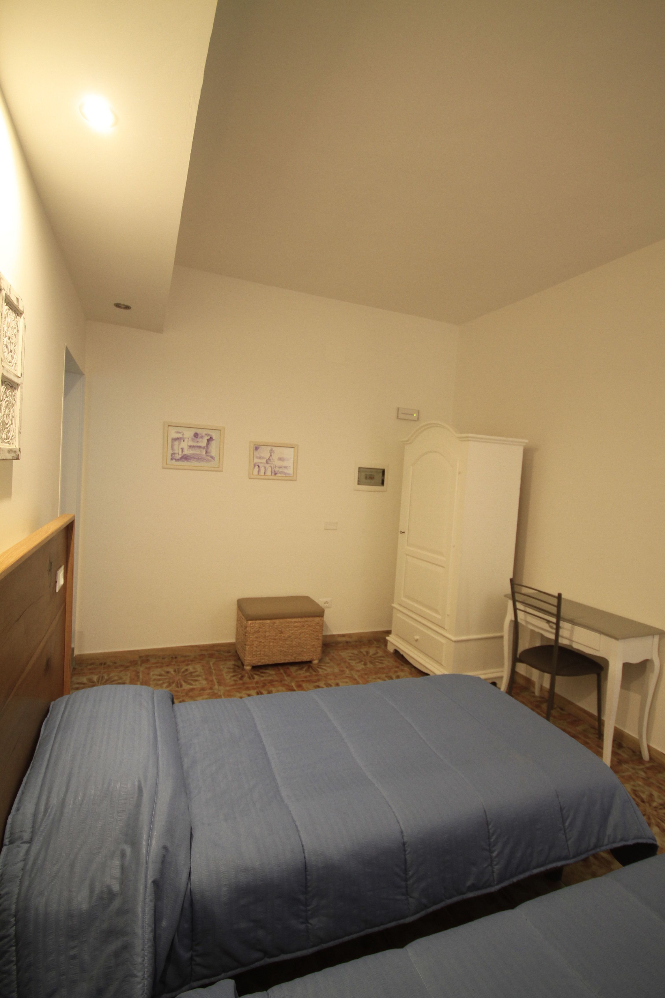 A bedroom with two beds, a desk, a chair, a wardrobe, and two wall-mounted pictures.