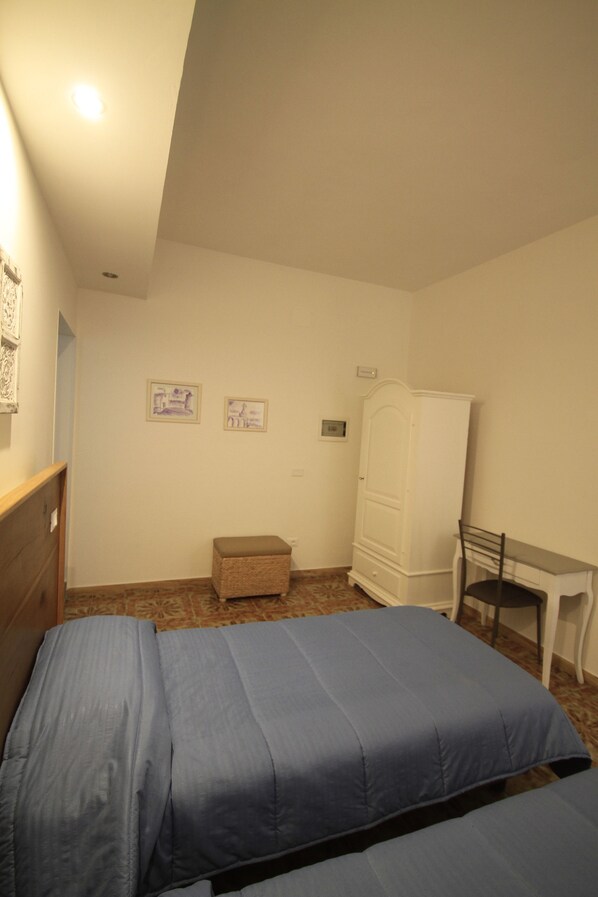 Un dormitorio con dos camas, un escritorio, una silla, un armario y dos cuadros colgados en la pared.