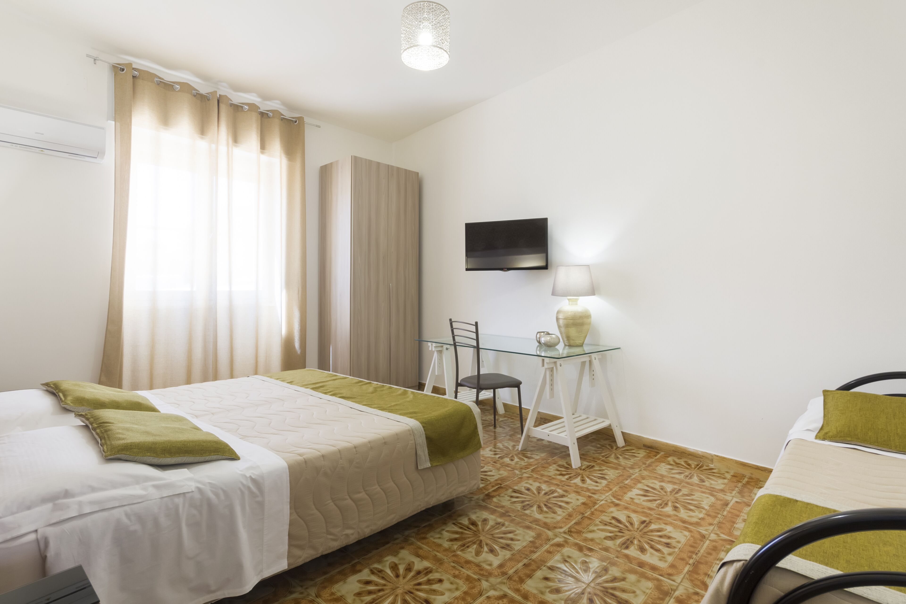 Una habitación de hotel con cama, escritorio, silla, televisor y lámpara.