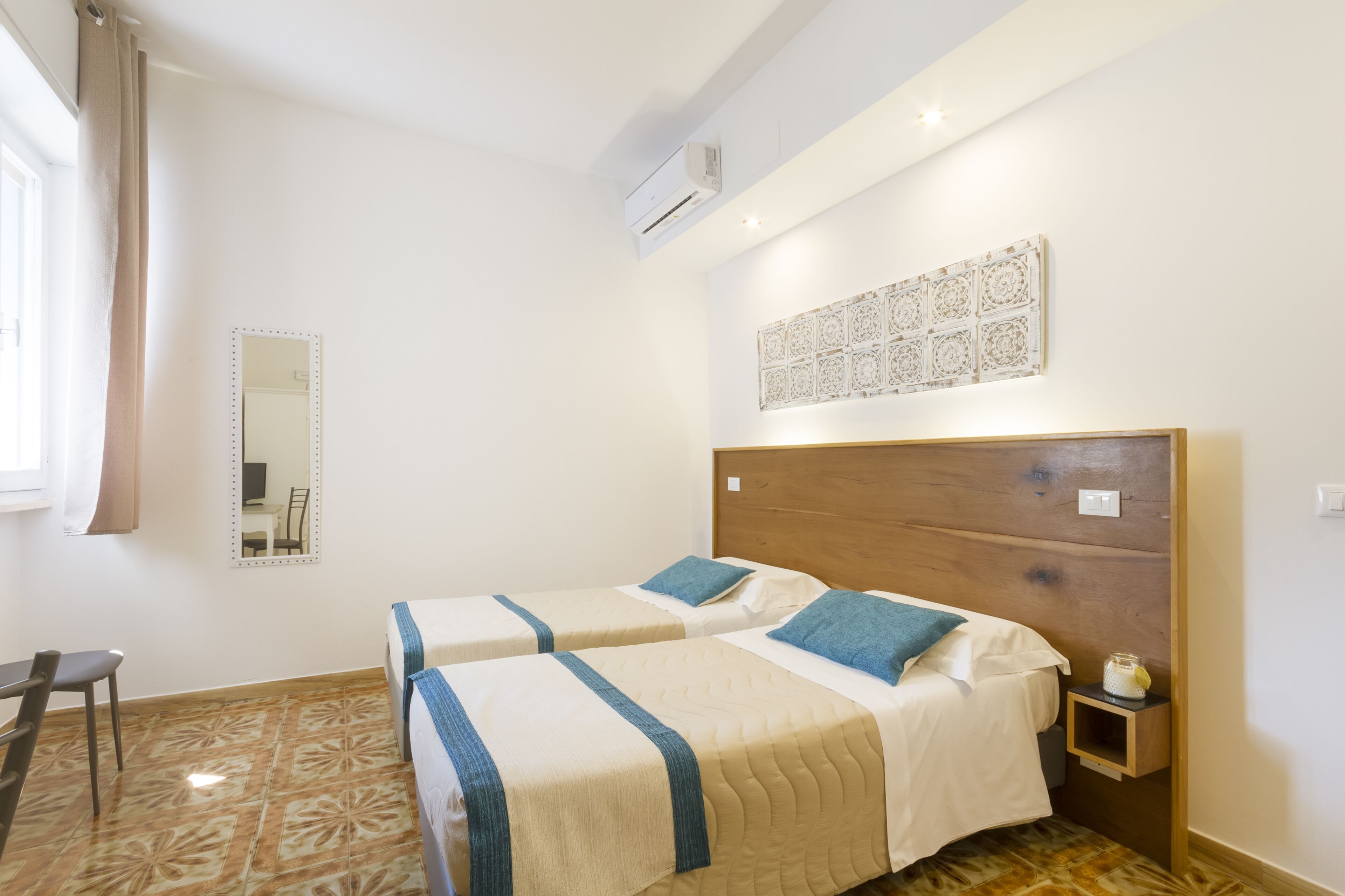 Habitación de hotel con dos camas, un espejo, aire acondicionado de pared y un adorno mural.