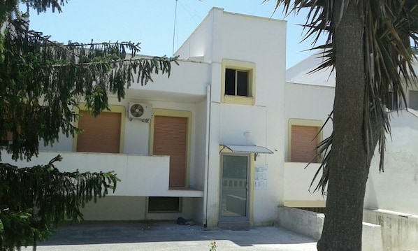 Un edificio con fachada blanca, un ventanal pequeño y una puerta con panel de vidrio.