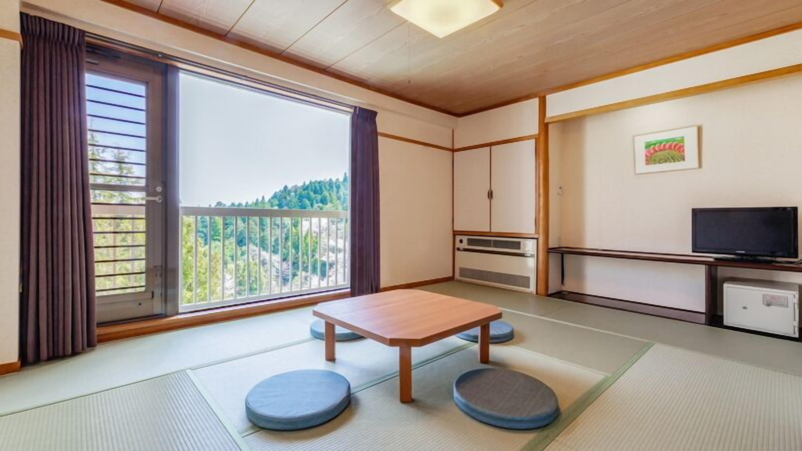 Una habitación con suelo de tatami, una mesa de madera baja, esteras de tatami, un televisor y vistas a un bosque a través de una puerta corredera.