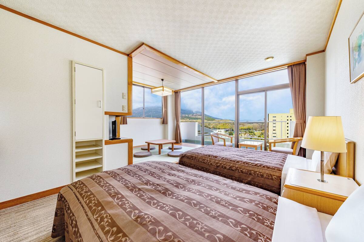 A hotel room with a large bed, a desk, a chair, a small table, and a view of the city.