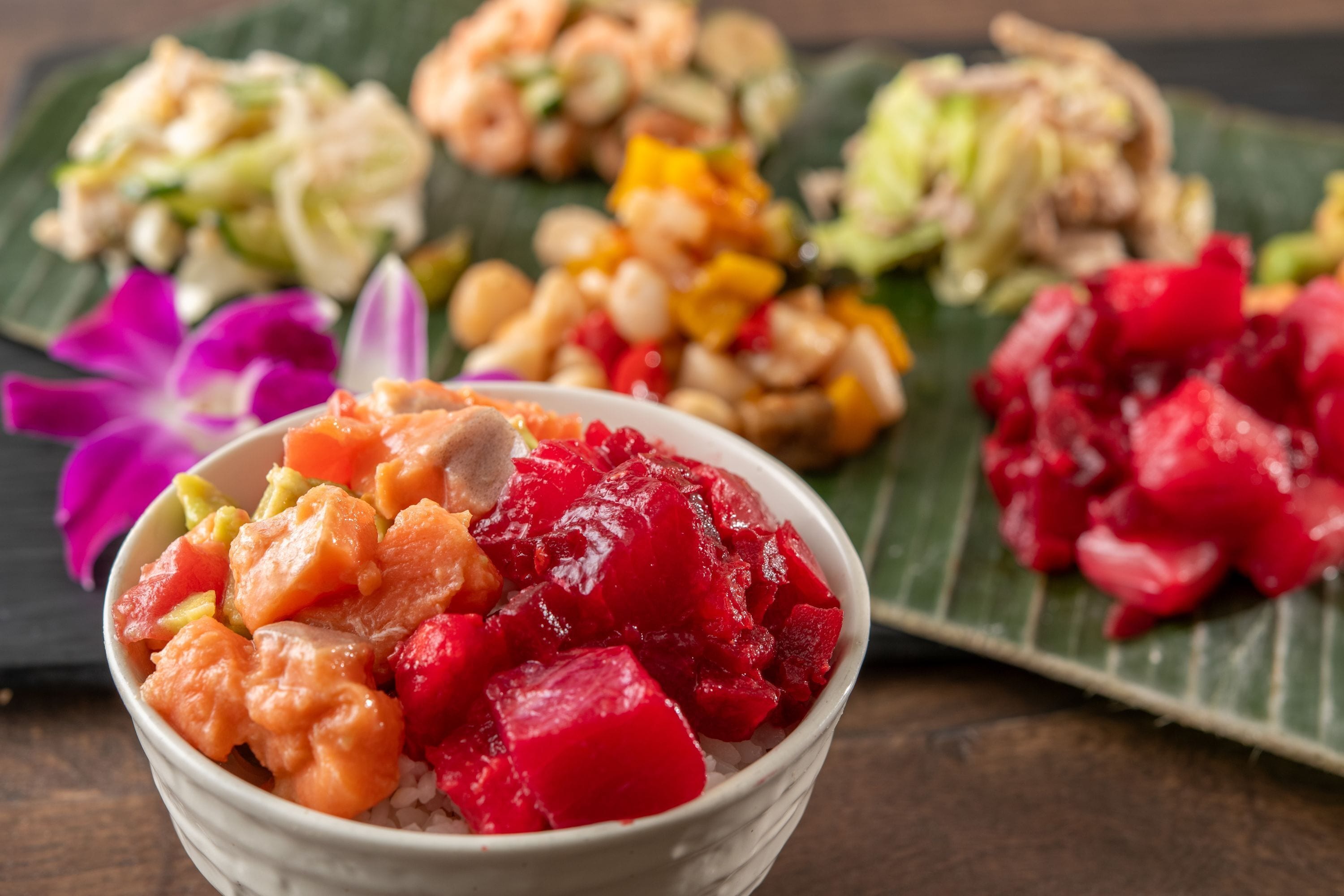 Uma tigela de comida colorida com camarão, vegetais e frutas vermelhas sobre uma folha verde.