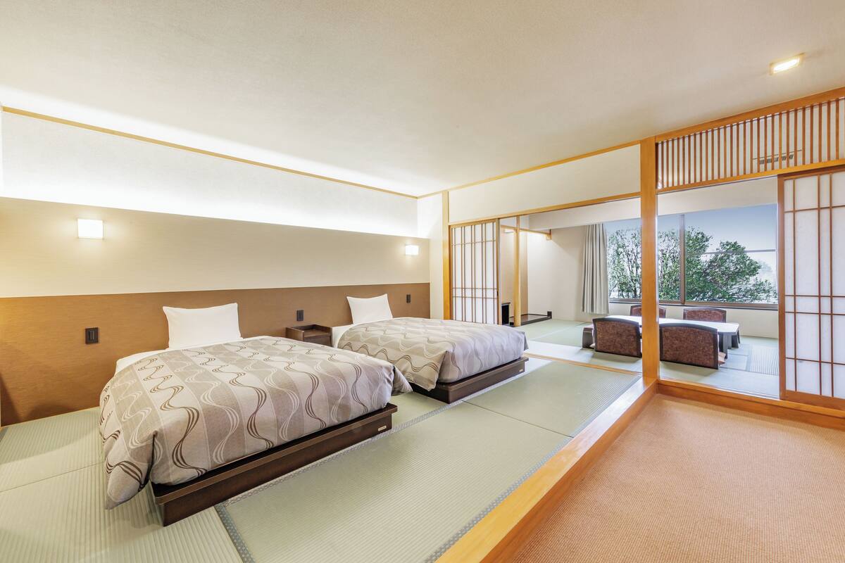 A hotel room with two beds, a tatami mat floor, a sliding door with a view, and a small table with chairs.