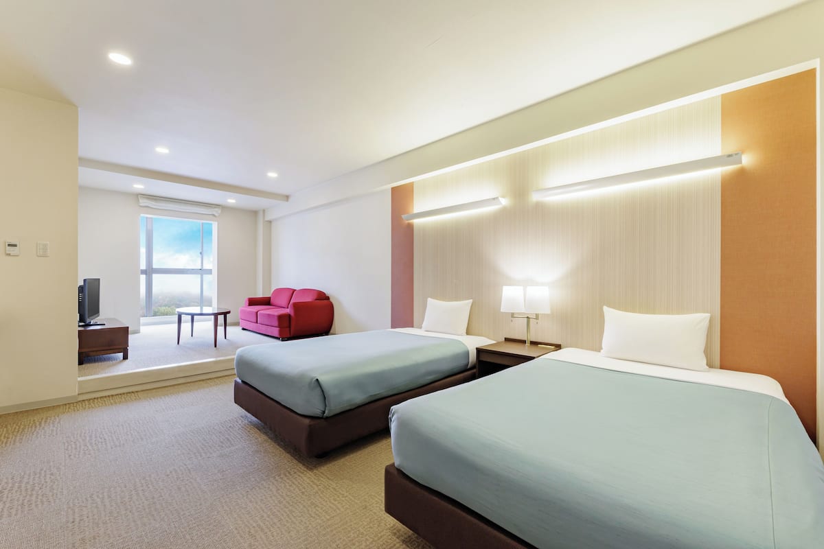 A hotel room with two beds, a TV, a red chair, and a window with a view.
