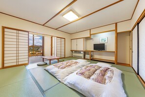 Una habitación japonesa tradicional con suelo de tatami, un futón, puertas correderas, un televisor y vistas al exterior.