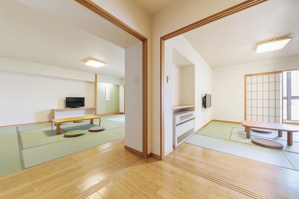 A traditional Japanese room with tatami flooring, a low wooden table, a bench, and a television on a shelf.