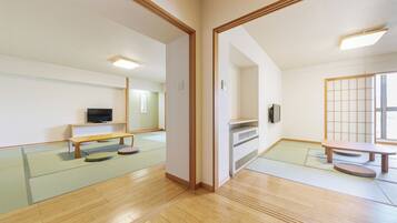 A traditional Japanese room with tatami flooring, a low wooden table, a bench, and a television on a shelf.