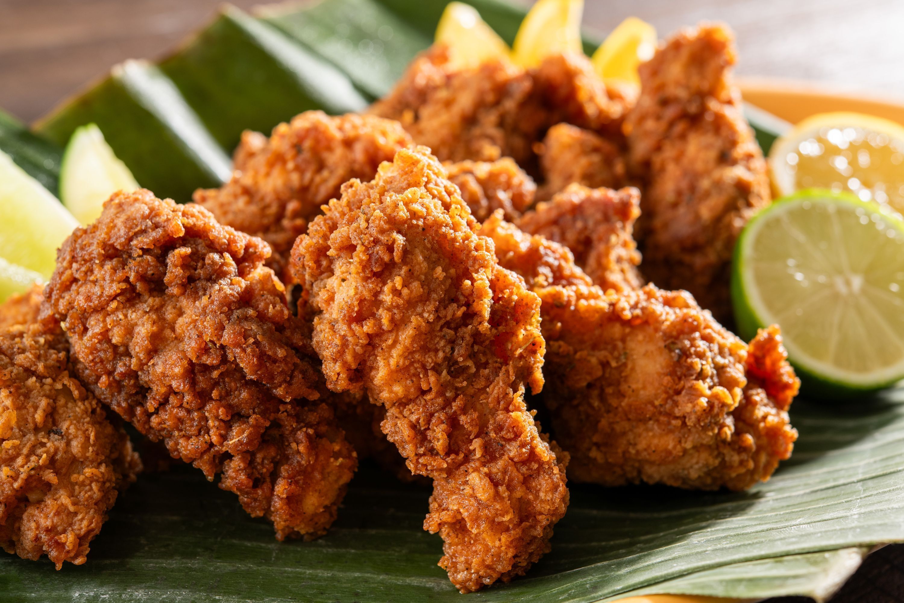 Fried chicken pieces on a banana leaf with lemon wedges.