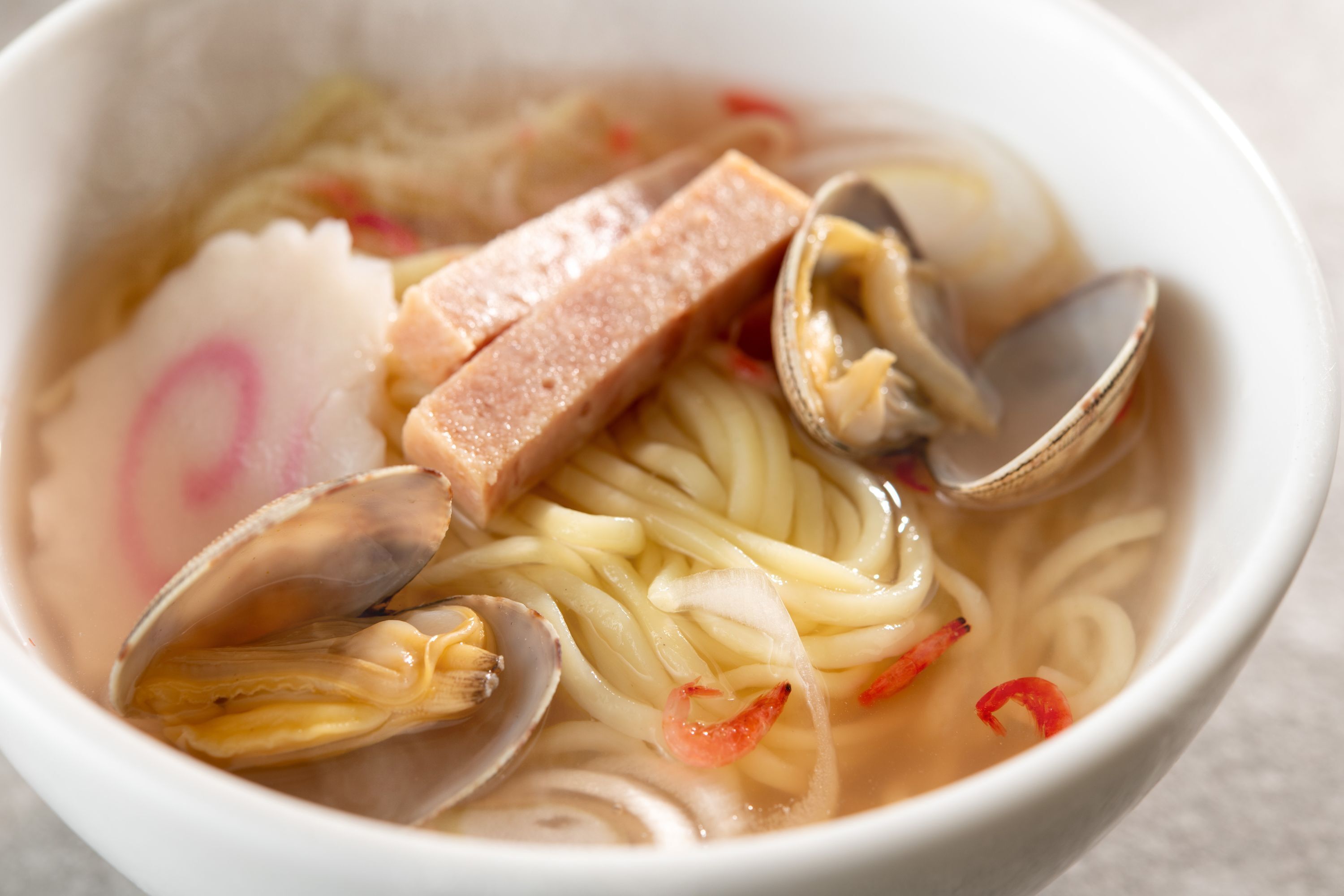 A bowl of ramen with noodles, clams, and a slice of meat.