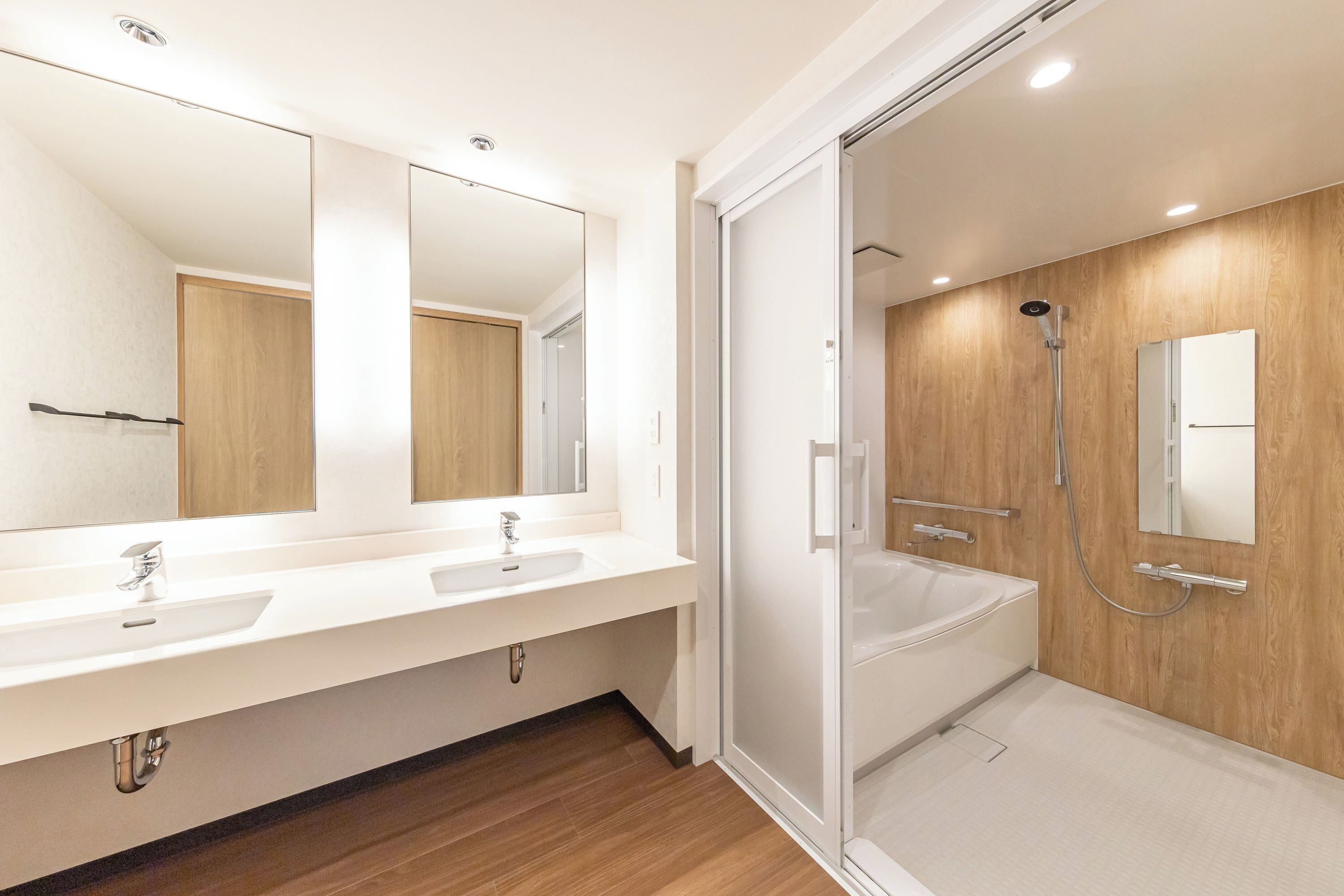A modern bathroom with two sinks, a large mirror, a shower enclosure, and wooden paneling.