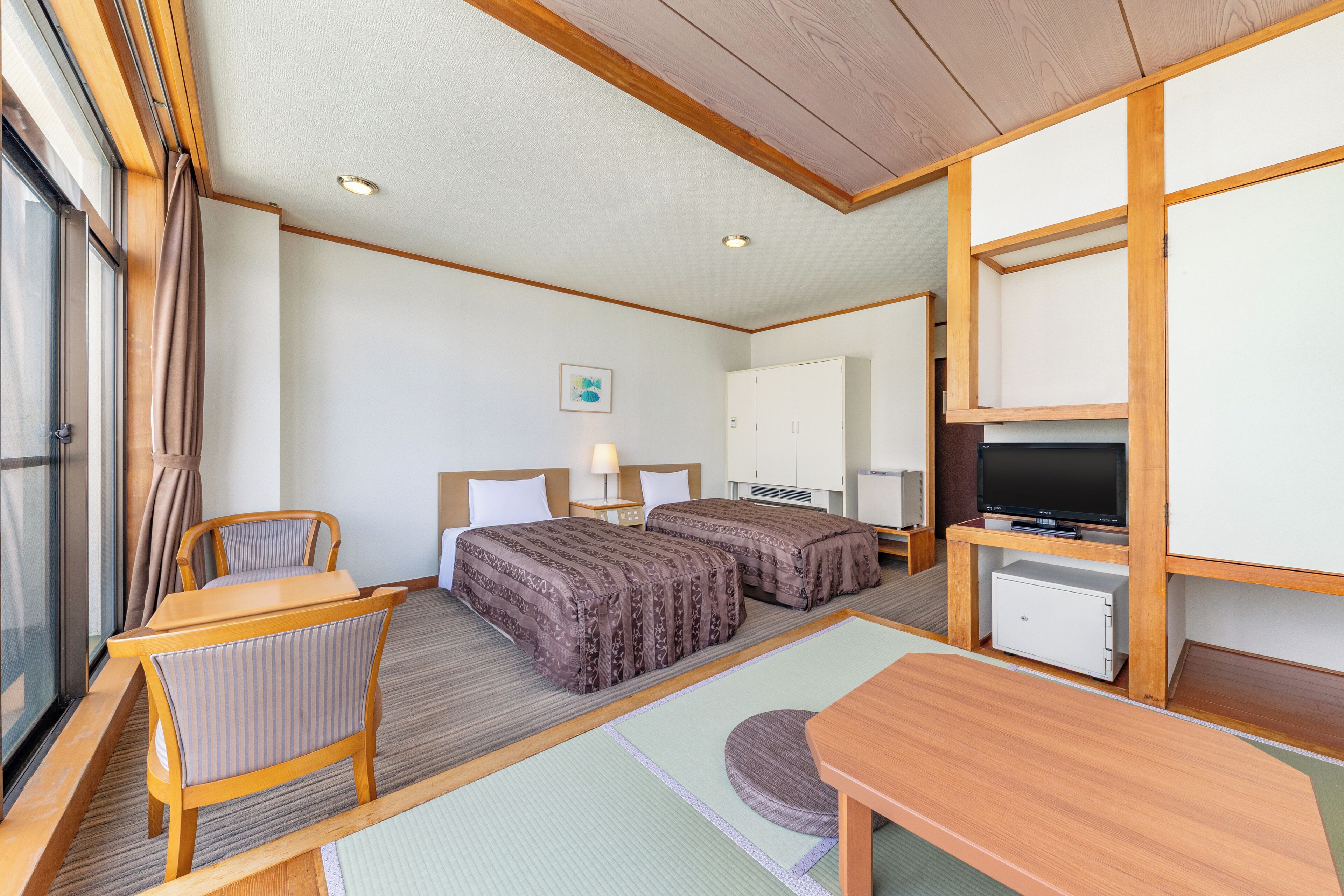 A hotel room with two beds, a TV, a desk, and a small refrigerator.