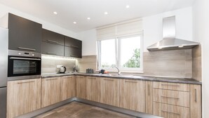 Een moderne keuken met houten kastjes, roestvrijstalen apparatuur en een groot raam dat natuurlijk licht binnenlaat.