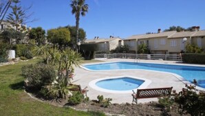 Una piscina rodeada por un jardín con palmeras y arbustos, con una hilera de edificios residenciales al fondo.