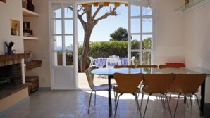 Un comedor con mesa y sillas, chimenea y vistas al exterior a través de amplios ventanales.