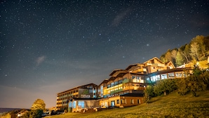 A large, multi-story hotel with a prominent 'natura' sign, situated on a hillside with a starry night sky above. - Natura Hotel Bodenmais (Bodenmais)