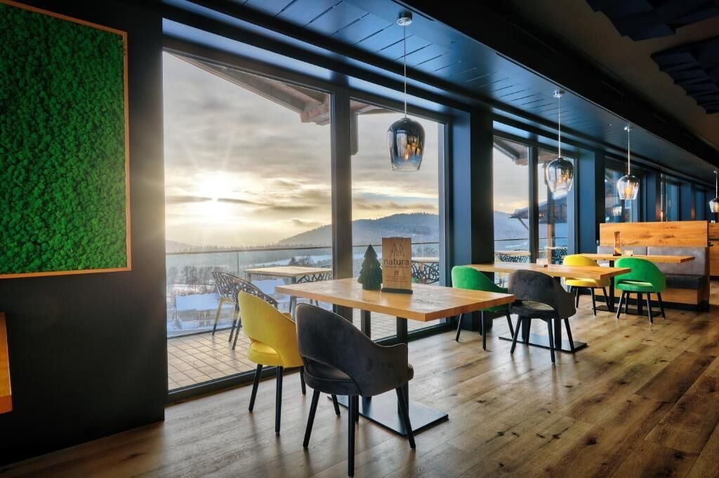 A restaurant with large windows, wooden tables, and chairs.