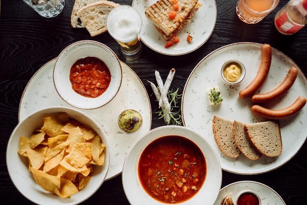 A table with various food items including chips, soup, sausages, and bread.