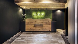 A reception desk with a wooden finish and a green wall behind it. - Natura Hotel Bodenmais (Bodenmais)