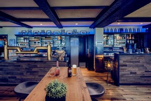 Eine Bar mit einem Holztisch, Barhocker sowie einer Auswahl an Flaschen und Gläsern.