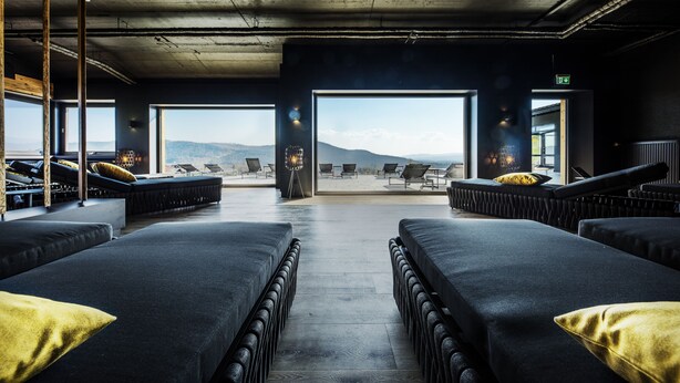 A modern spa area with two large massage beds, a view of the mountains, and a seating area with chairs and a table. - Natura Hotel Bodenmais (Bodenmais)