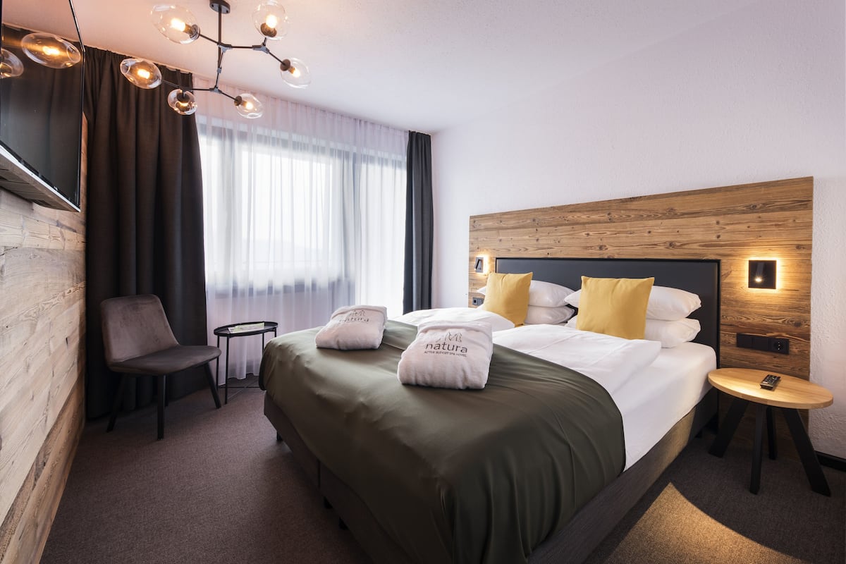 A hotel room with a large bed, a small table, a chair, and a TV on the wall.