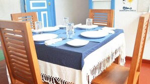 Una mesa de comedor con platos, vasos y mantel azul, rodeada de sillas de madera.