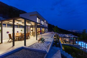 A modern house with a covered patio, outdoor dining area, and a swimming pool.