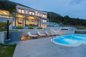 A modern house with a swimming pool, outdoor seating, and a well-lit patio area.