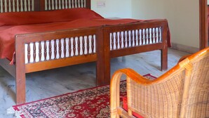 Una habitación con una cama de madera, una silla de mimbre, un tapete con estampado rojo y blanco y cuadros en las paredes.