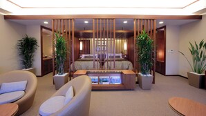 A modern hotel room with a bed, two potted plants, a seating area with chairs, and a small table.