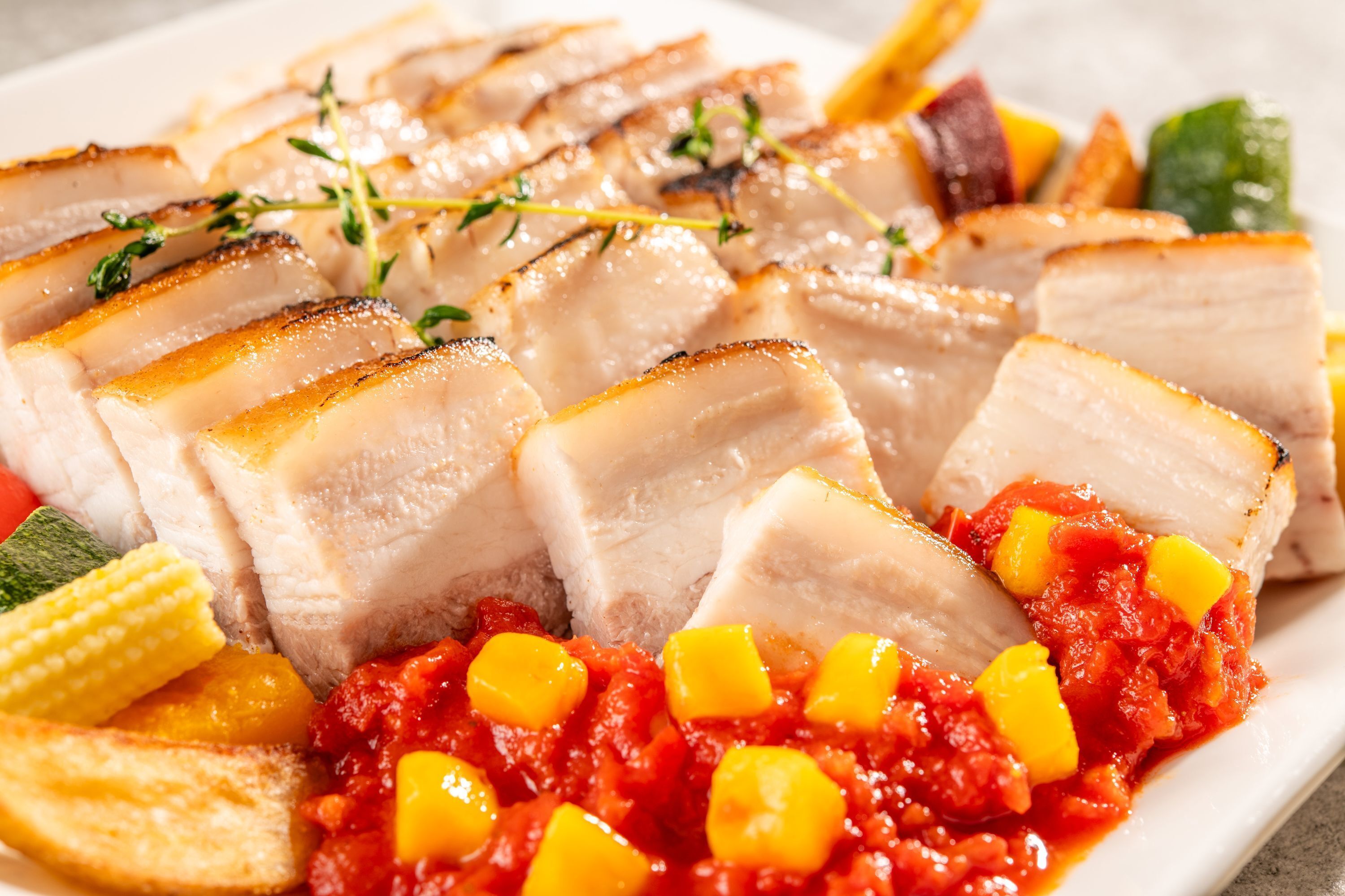 A plate of sliced meat with vegetables and a tomato-based sauce.