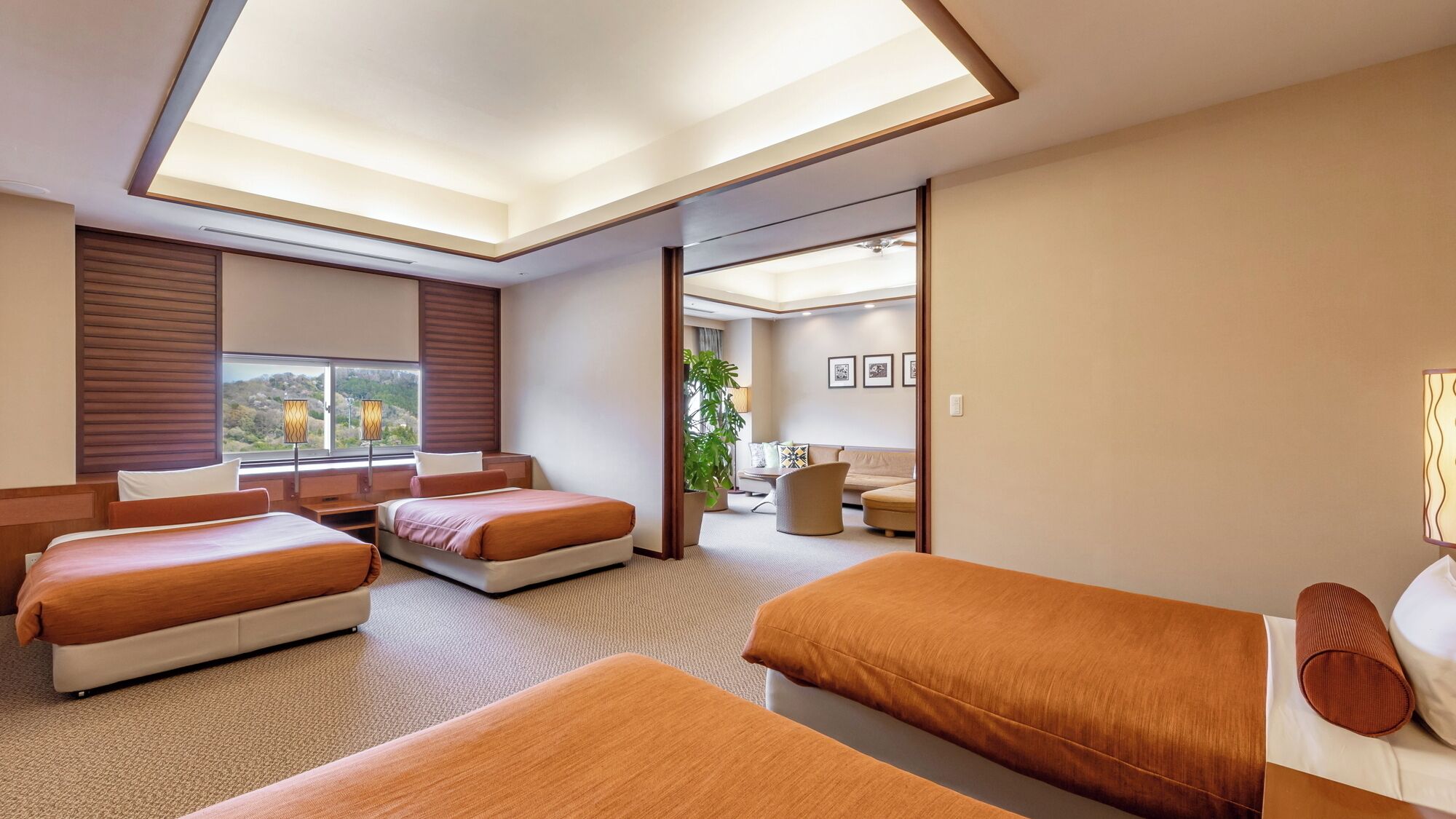 A hotel room with a large bed, a smaller bed, a sofa, a desk, and a plant.