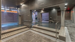 A modern indoor pool area with tiled steps leading to the water, a glass barrier, and a brick wall.