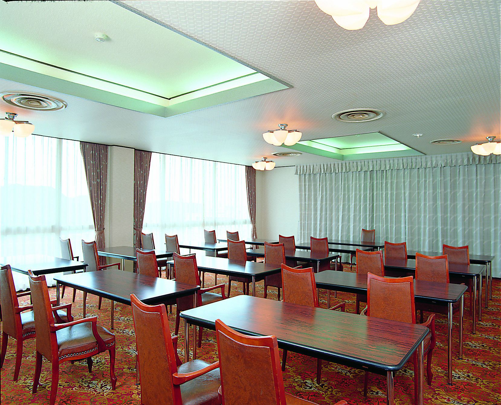 A conference room with multiple tables and chairs, large windows with curtains, and a patterned carpet.