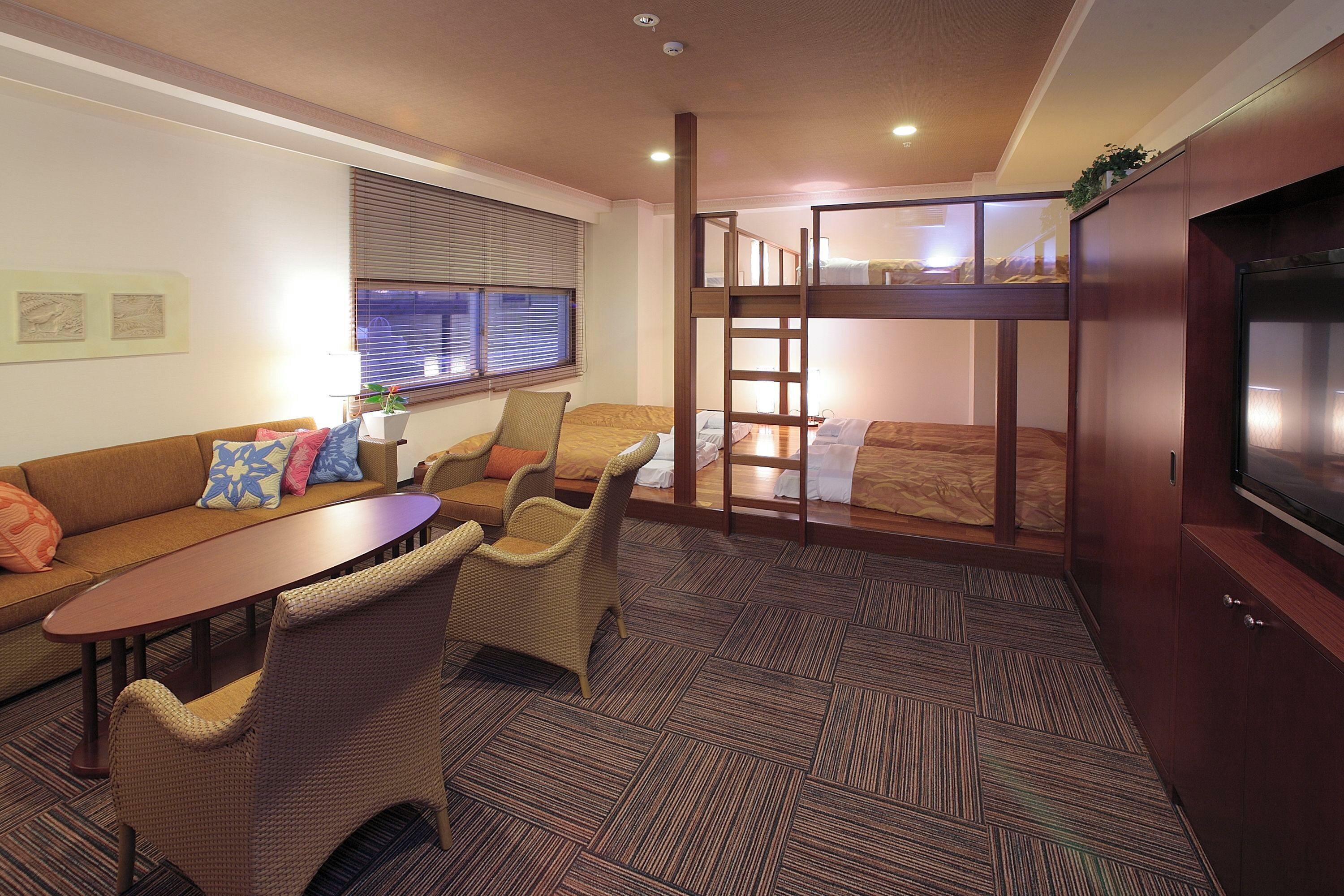 A compact hotel room with a bunk bed, a sofa, a dining table, and a TV.