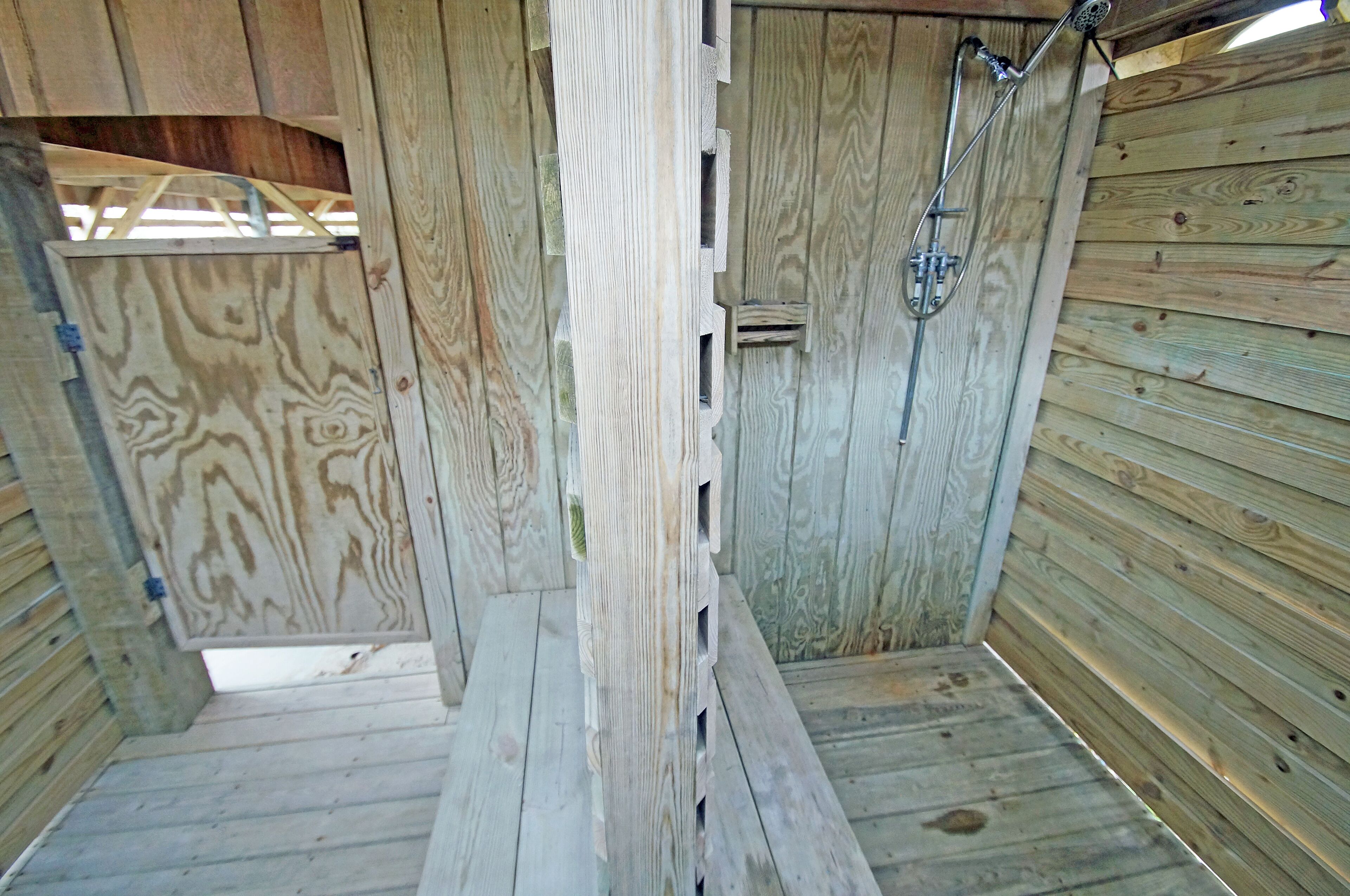 Una cabaña de madera con ducha, un banco y un ventanal pequeño.