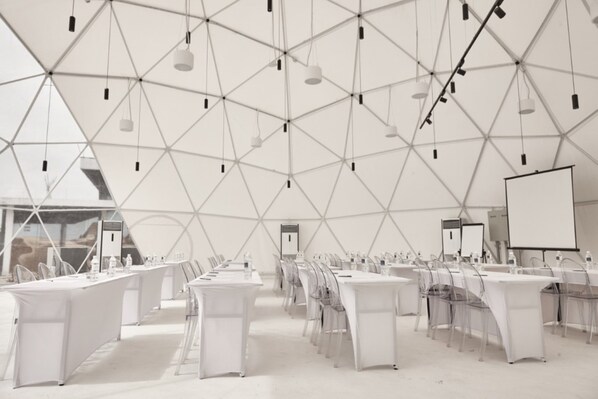 A conference room with white tables and chairs, a whiteboard, and a projector screen.