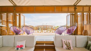 A modern hotel room with a large window, two cushioned sofas, and two purple woven chairs. - The ANMON Resort Bintan- Glamping (Bintan)