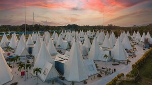 A large number of white tents arranged in rows on a sandy ground with palm trees in the background. - The ANMON Resort Bintan- Glamping (Bintan)