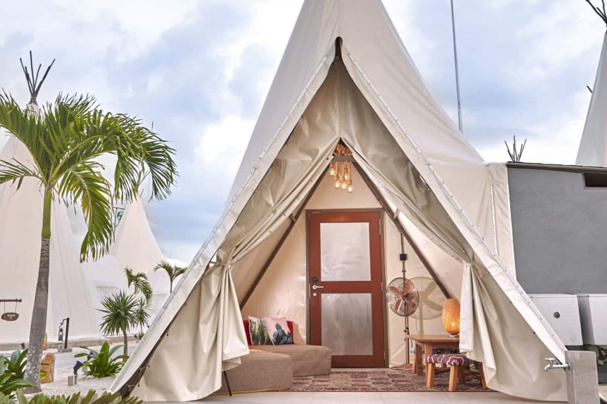 A teepee-style accommodation with a central door, a seating area with cushions, and a small table.