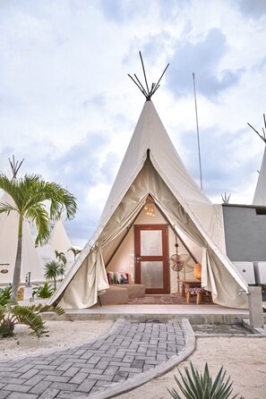 A teepee-style accommodation with a central door, a seating area with cushions, and a small table. - The ANMON Resort Bintan- Glamping (Bintan)