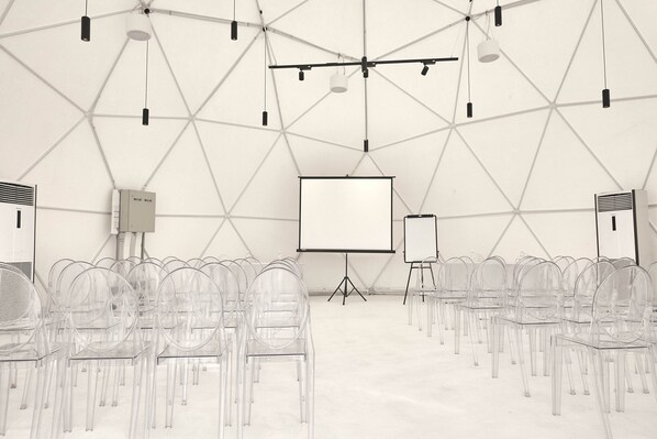 A large, geometrically patterned room with clear chairs arranged in rows, a projection screen, and a whiteboard. - The ANMON Resort Bintan- Glamping (Bintan)