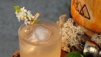 Un vaso de una bebida clara con adorno, mitades de lima y un coco sobre una superficie de madera.