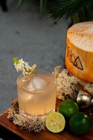 Un vaso de una bebida clara con adorno, mitades de lima y un coco sobre una superficie de madera.