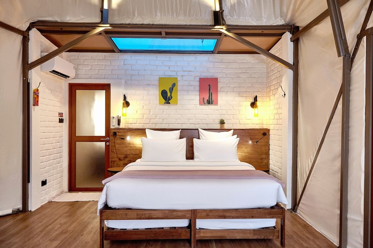 A tent-style bedroom with a wooden bed, white bedding, and two wall-mounted lights.