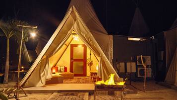 A tented accommodation with a warm interior, a door, a table with a fire, and a fan.