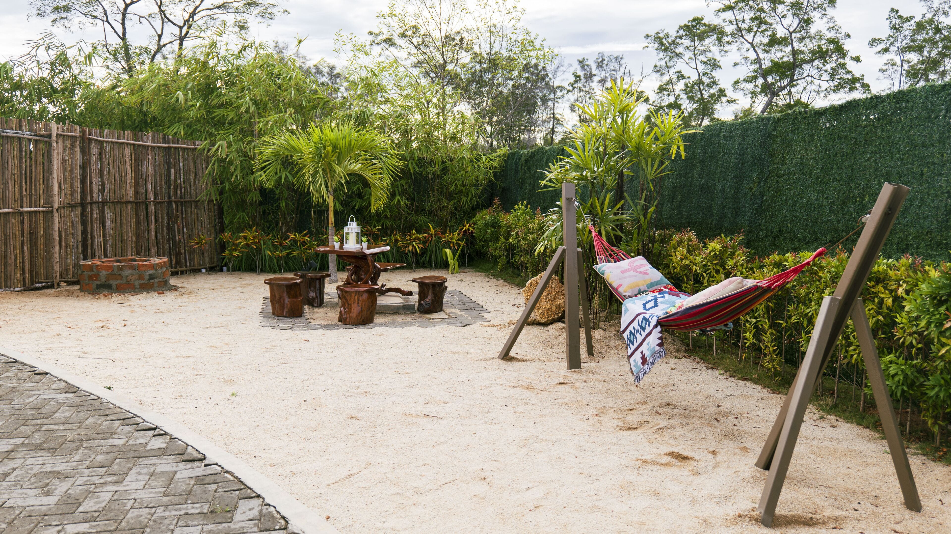 A sandy outdoor area with a wooden table, chairs, and a hammock.