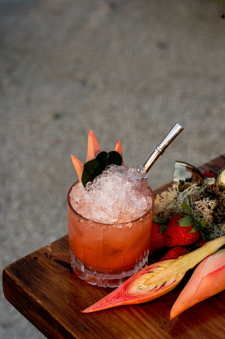 A cocktail in a glass with a metal straw, surrounded by ice, on a wooden surface.